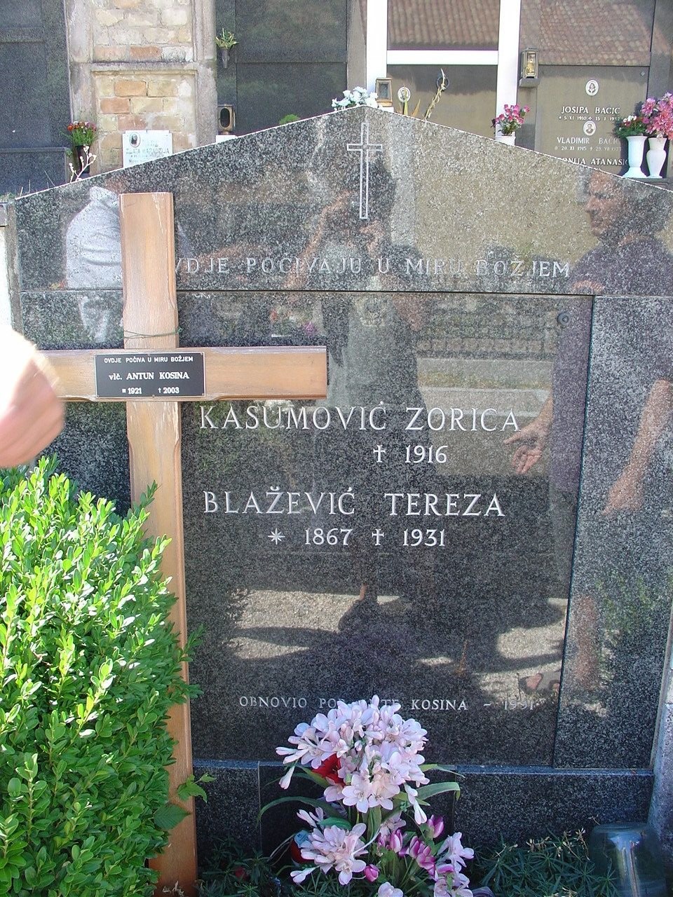 A granite tomb in Senj cemetery reading KASUMOVIĆ ZORICA and BLAŽEVIĆ TEREZA, with a
             wooden cross standing in front of it